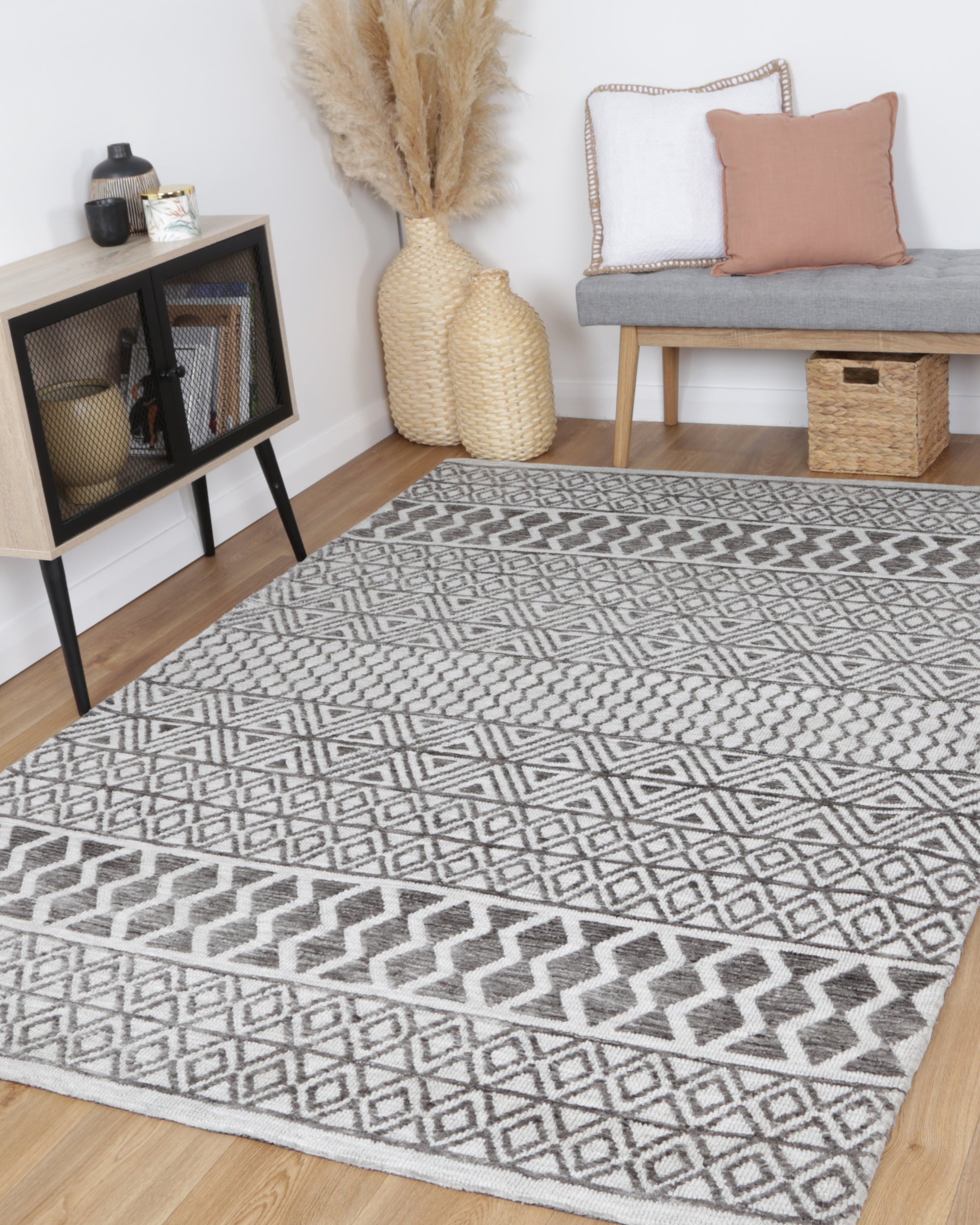 Alayah Tessellations silver Rug in living room with light flooring and a grey chair and woven accessories