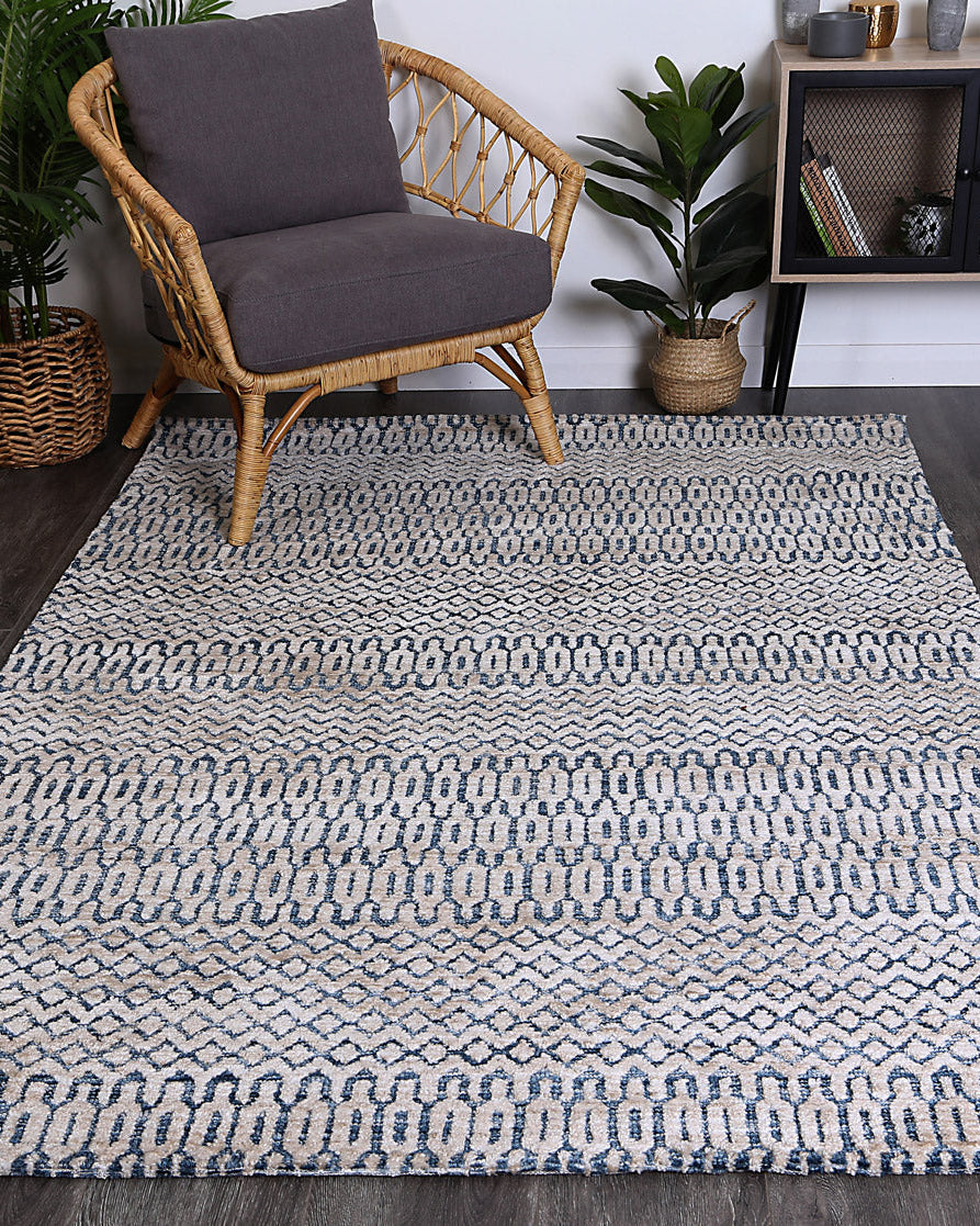 Alayah Camphils Blue Rug in living room on dark flooring with wicker and grey chair