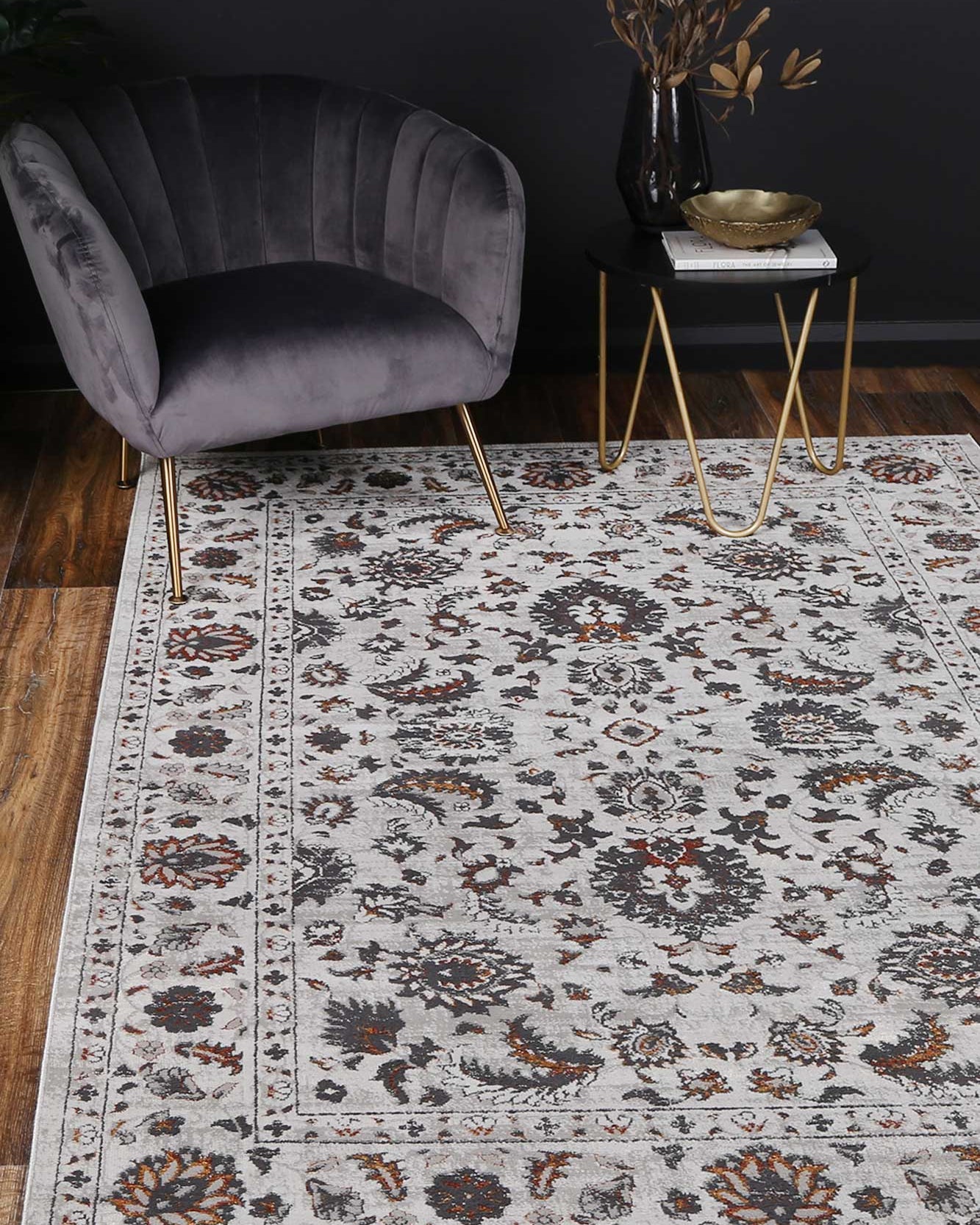 Almada Charcoal Floral Rug in lounge room with grey velvet chair on natural wood floors, with gold and brass accessories