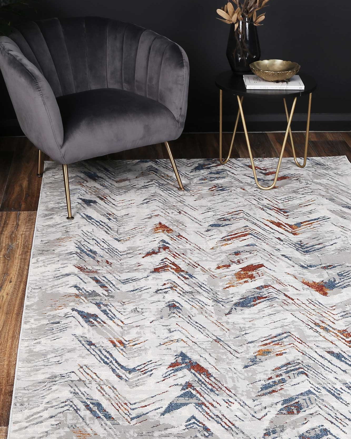 Almada silver and Multicoloured herringbone Rug, with charcoal velvet arm chair, dark walls on natural timber flooring